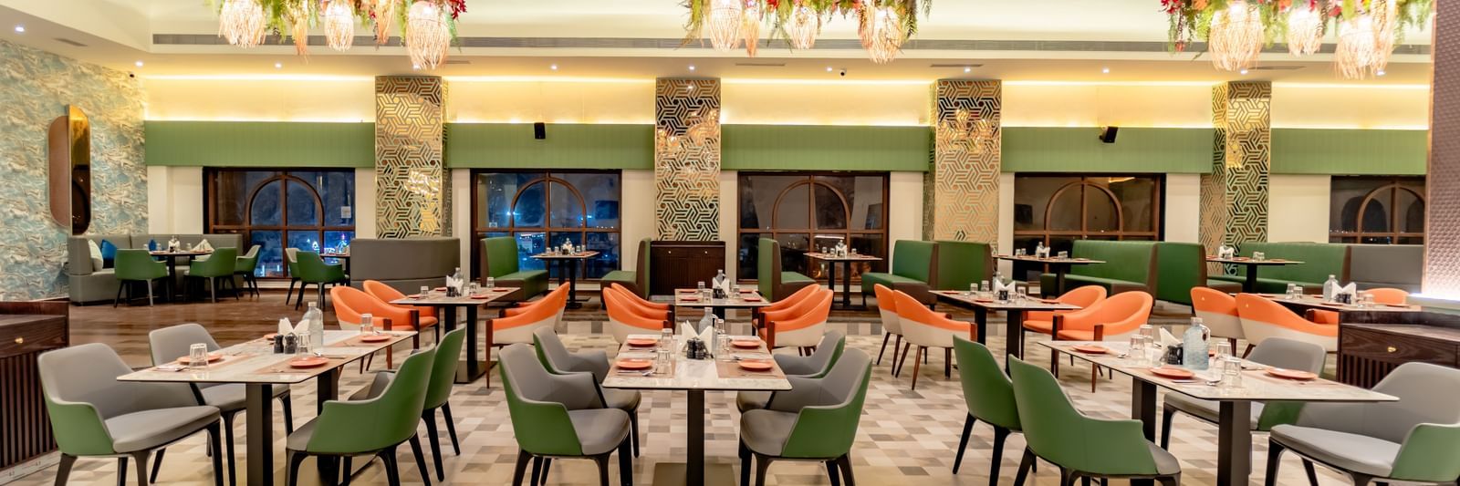 The dining area with green and orange chairs and decorative hanging elements | Pravasa Hotel, Vijayapura