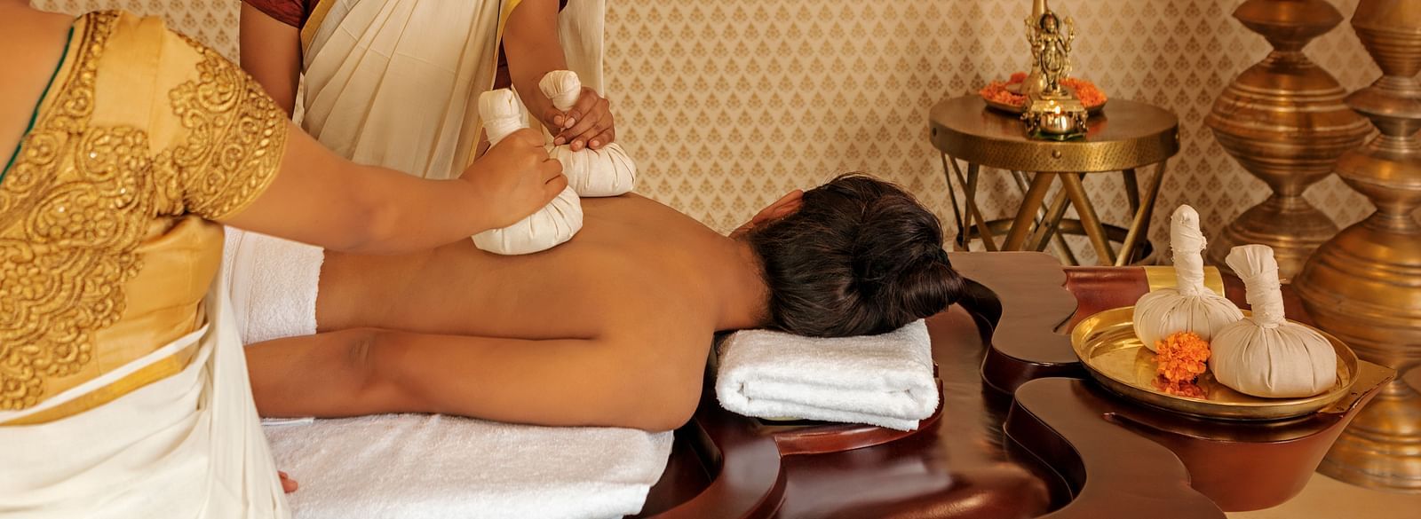 A person receiving a massage with another person standing nearby, indoor setting with decorative items - Shreyas Retreat