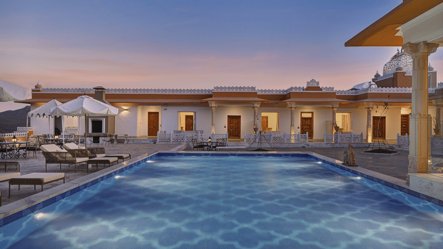 Overview of a swimming pool at Khas Mahal Suites, Udaipur with a backdrop of warm lit property.