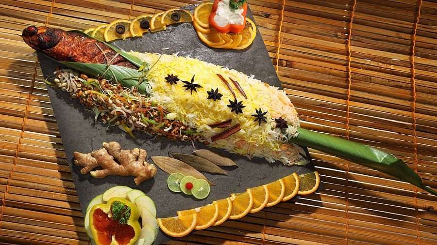 A non-veg platter featuring fish wrapped in a banana leaf, served at Aambal Restaurant, with its name highlighted on the wall in the background at Uday Backwater Resort