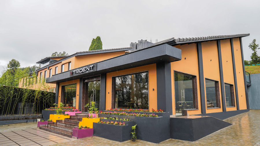 Exterior view of a modern orange building with grey trim, featuring glass walls and vibrant flower boxes at the entrance at Trident The Boutique Hotel, Ooty.