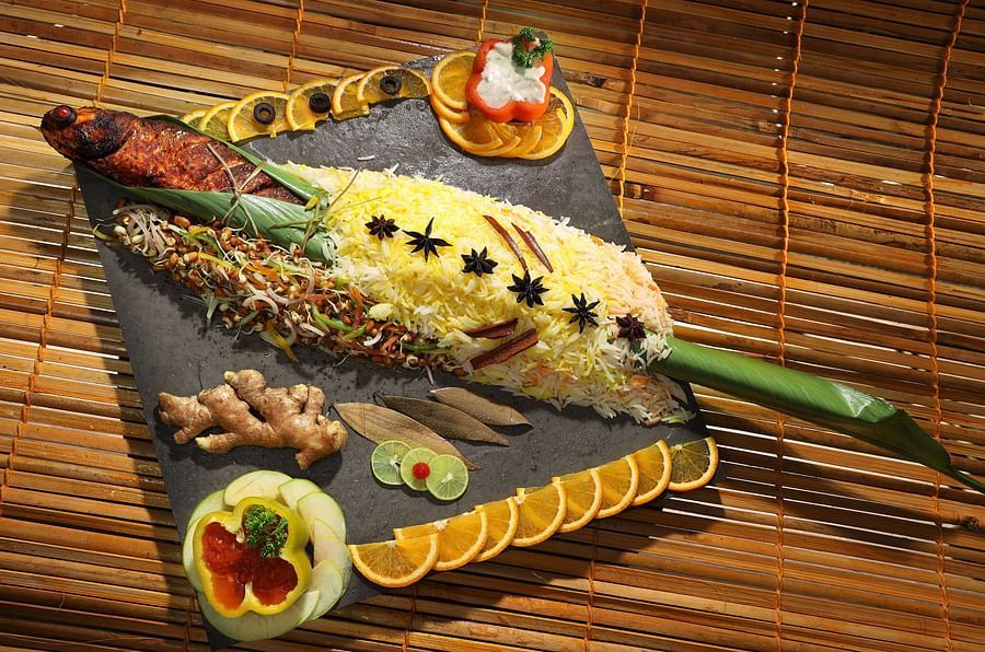A non-veg platter featuring fish wrapped in a banana leaf, served at Aambal Restaurant, with its name highlighted on the wall in the background at Uday Backwater Resort