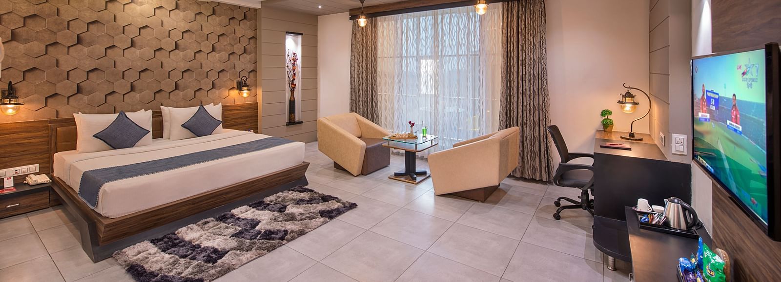 Spacious hotel room with a large bed, ambient lighting, and sliding glass doors opening to a balcony at Lords Eco Inn Morbi.