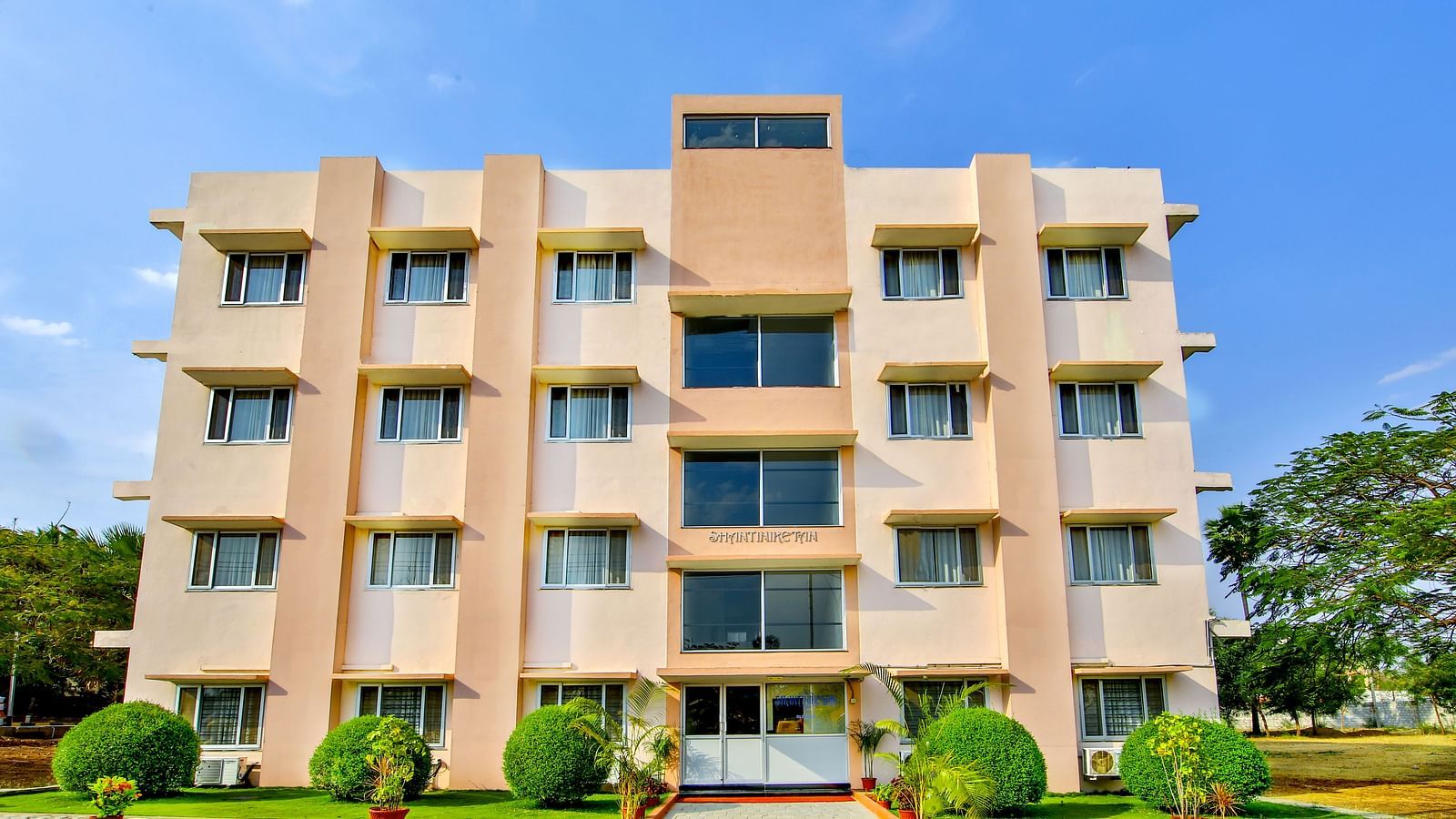 Four-story building with a pink and beige exterior, front view with a clear blue sky background at Greens Inn - Modern Hotel in Hyderabad.