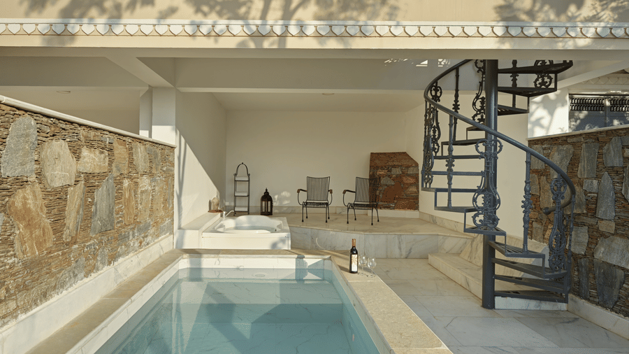 Plunge Pool Suite with Jacuzzi at Fateh Safari Suites, Kumbhalgarh featuring a small pool, bathtub next to it, two chairs, a bottle of wine, and two glasses.