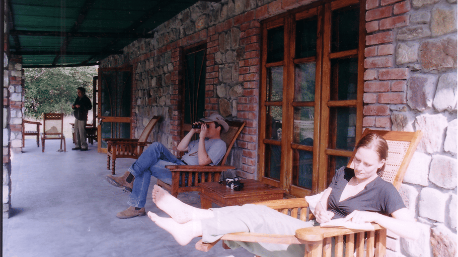 People relaxing on wooden lounge chairs along a stone-walled porch veranda.