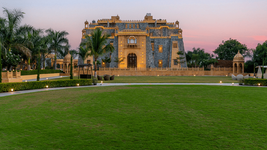 A wide evening view of the green lawn and the facade of EsthereaRaj Leela, Ranakpur.