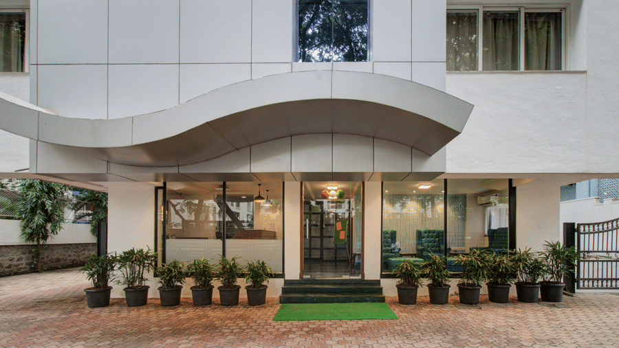 The building entrance with glass doors, potted plants, and tiled driveway area. | Magnus Riverside Exterior