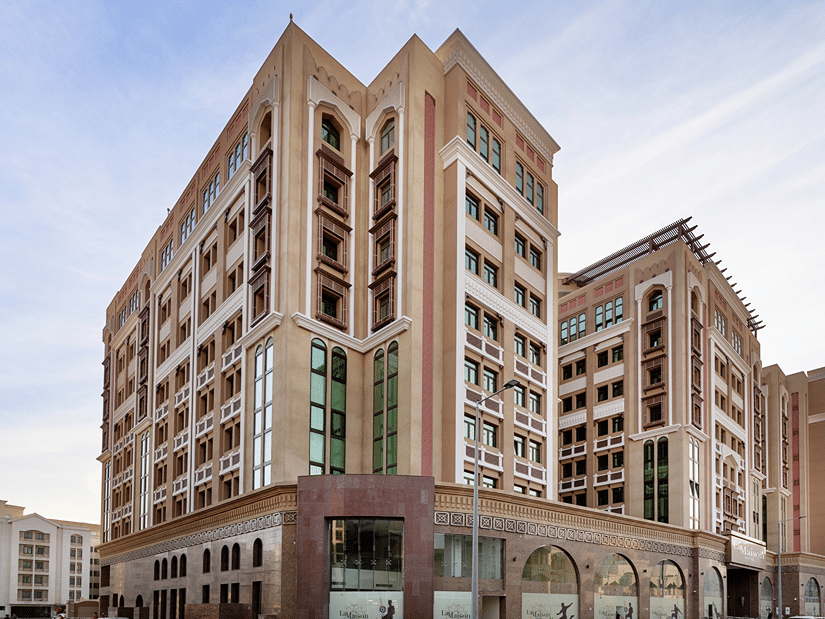 Facade view of La Maison Hotel, Doha, featuring three towers and a blue sky in the background, a hotel near Doha Corniche.