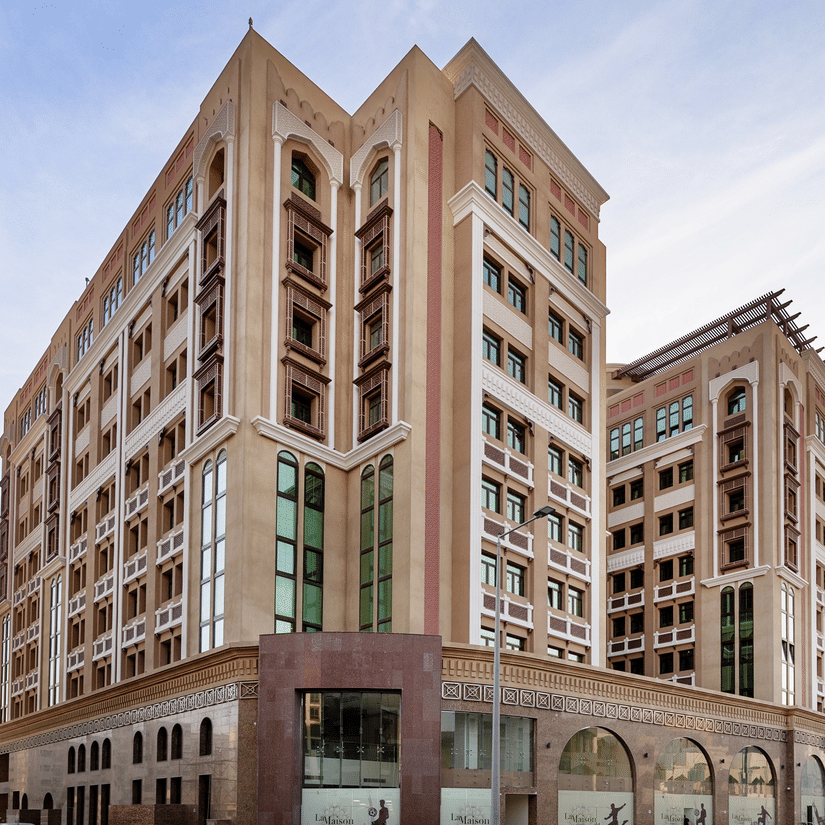 Facade view of La Maison Hotel, Doha, featuring three towers and a blue sky in the background, a hotel near Doha Corniche.