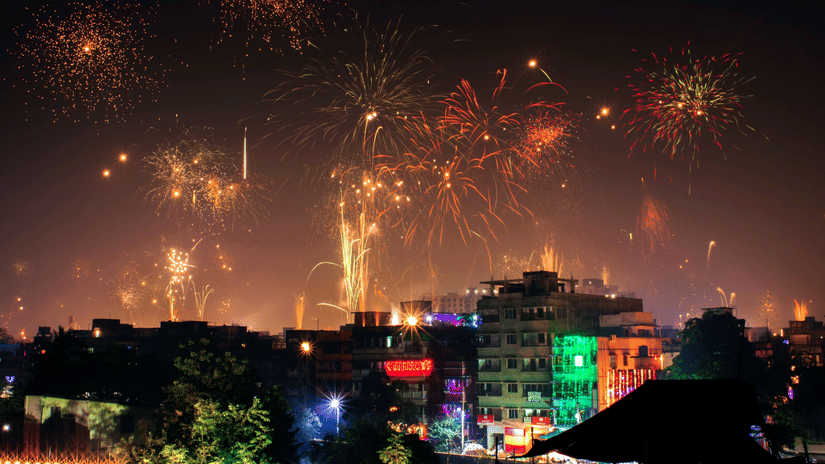 Beautiful firecrackers covering the entire night sky with buildings decorated with string lights in the foreground.