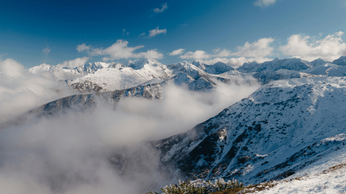 Vast mountain landscape with snow-covered peaks rising above a thick layer of low-lying clouds under a clear sky.