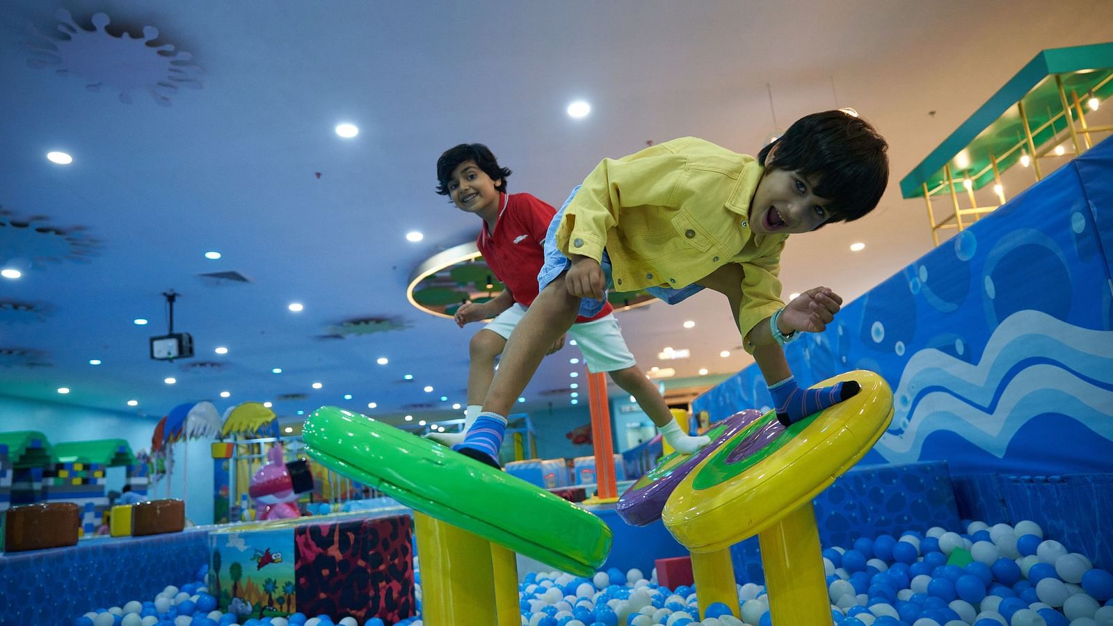 Children playing on a climbing structure in a large ball pit, surrounded by colorful balls.
