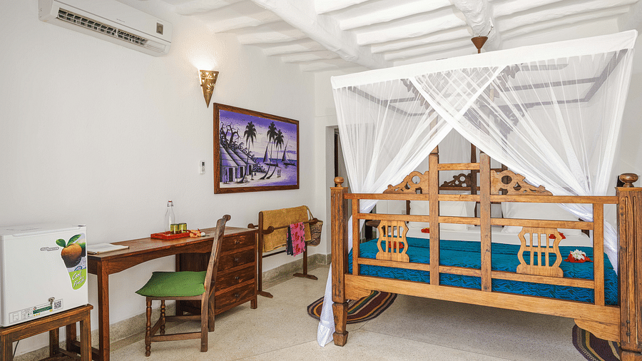 Bright bedroom with a wooden bed draped in a white mosquito net, desk, chair, a portrait on the wall - Shooting Star Boutique Hotel.