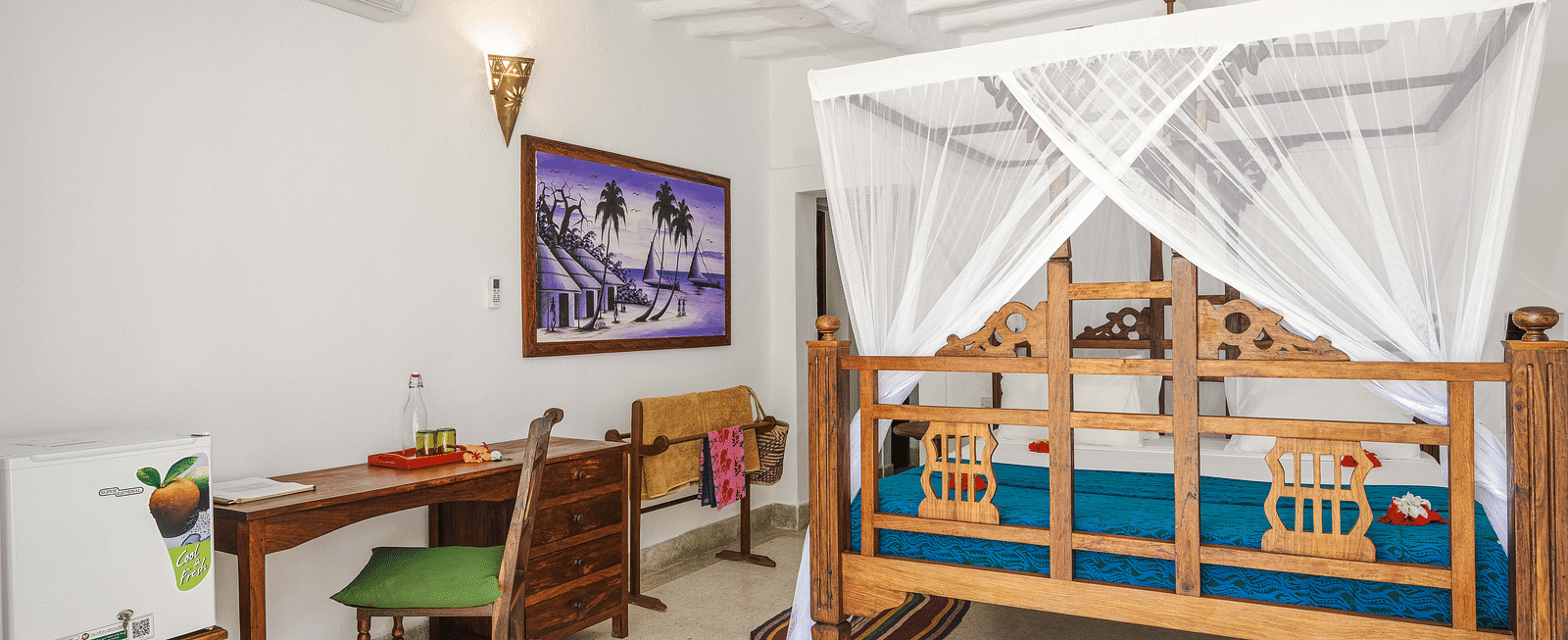 Bright bedroom with a wooden bed draped in a white mosquito net, desk, chair, a portrait on the wall - Shooting Star Boutique Hotel.