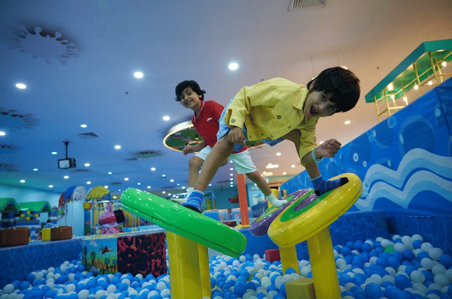 Children playing on a climbing structure in a large ball pit, surrounded by colorful balls.