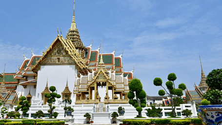 Overview of the grand palace in Bangkok, one of the Bangkok Sightseeing places, with a garden in front of it and blue sky in the background.
