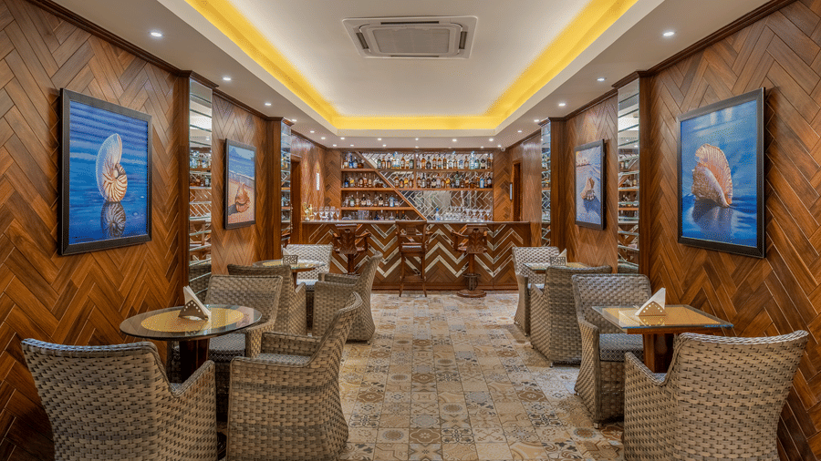 Elegant indoor bar at MAYFAIR Heritage, Puri featuring warm wooden interiors, cosy seating, patterned flooring, and a fully stocked premium liquor counter.