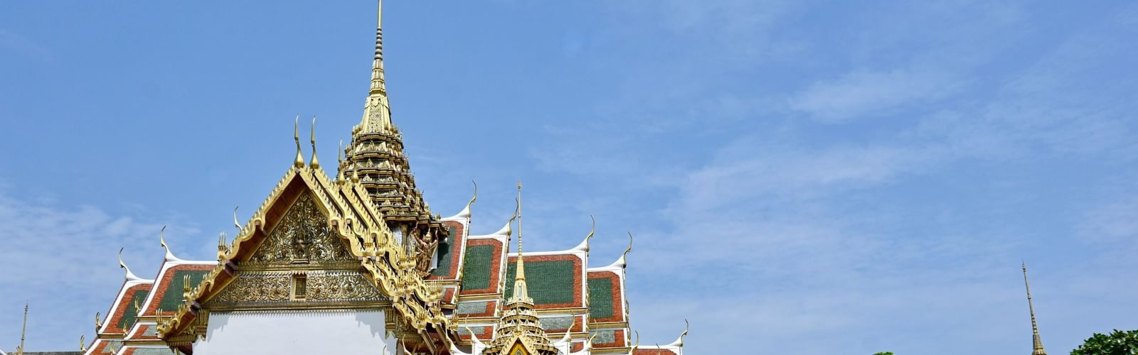 Overview of the grand palace in Bangkok, one of the Bangkok Sightseeing places, with a garden in front of it and blue sky in the background.