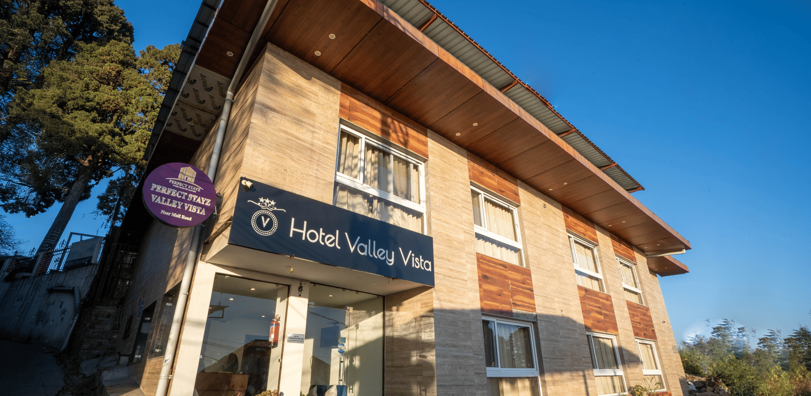 The exterior of a 2-storey hotel building with a slanted roof, a sign with hotel name as seen from a low angle on a sunny day | Perfectstayz Value Valley Vista