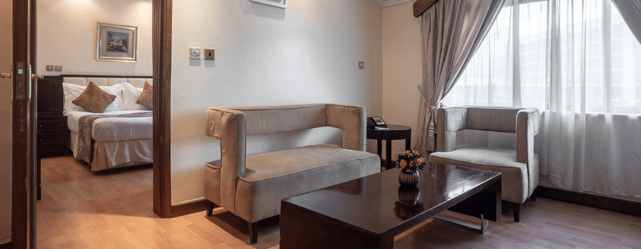 Living room of Suite at Boma Inn Nairobi featuring a sofa set placed by the window around a coffee table under with a wall hanging over it on the wall