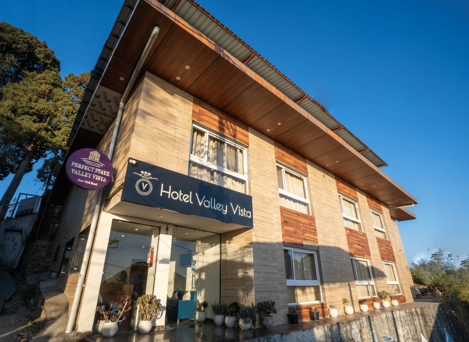 The exterior of a 2-storey hotel building with a slanted roof, a sign with hotel name as seen from a low angle on a sunny day | Perfectstayz Value Valley Vista
