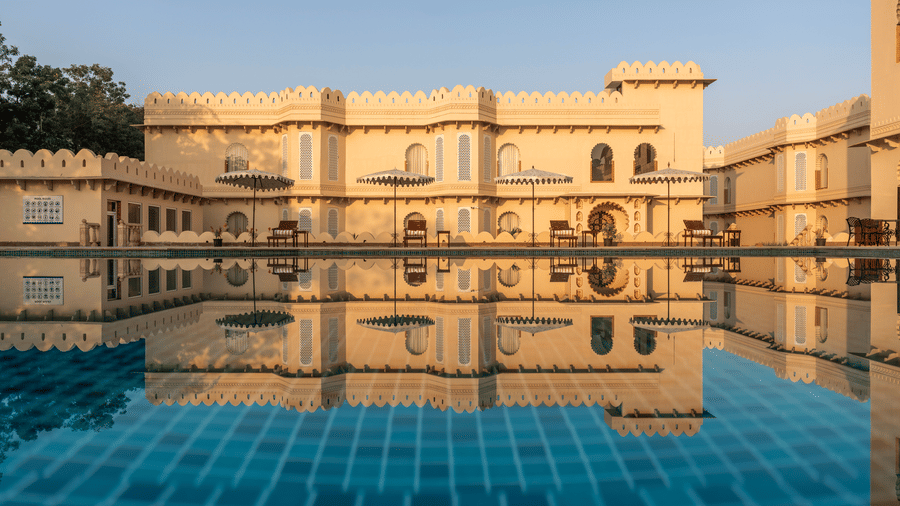 Grand facade of Kesar Bagh Palace, Chittorgarh, reflected in the still blue waters of the outdoor swimming pool at golden hour.