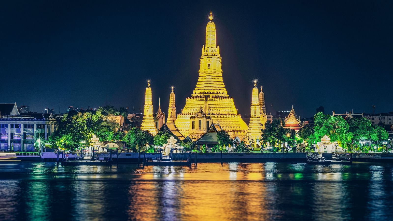 a temple in Bangkok illuminated with lights surrounding it next to a waterbody