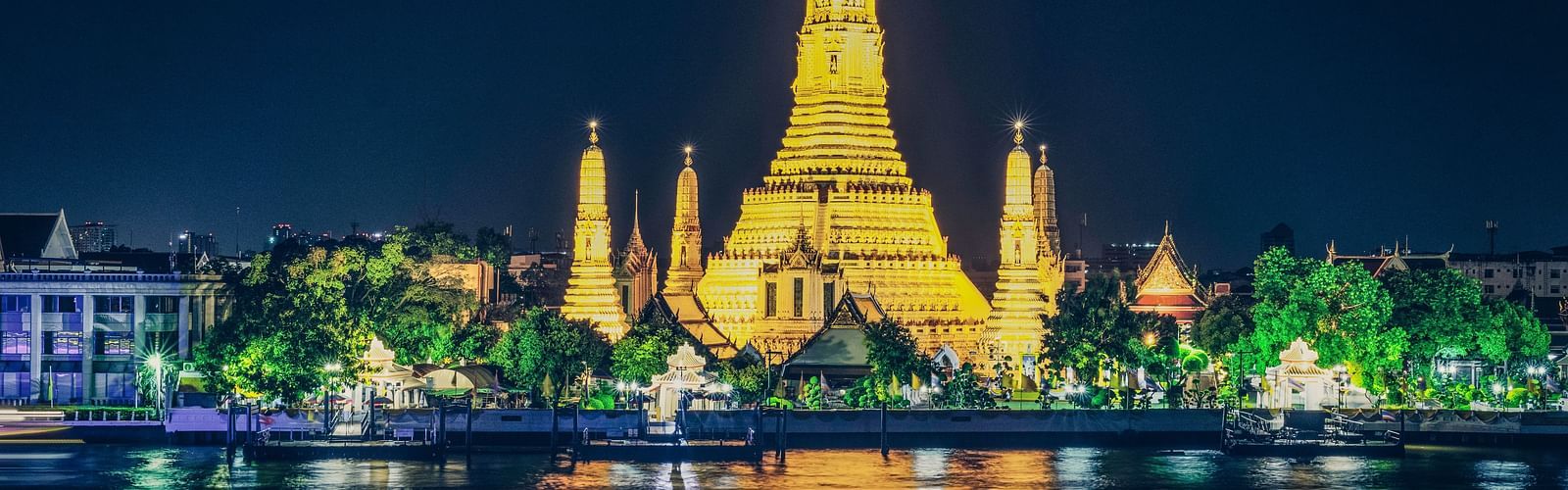 a temple in Bangkok illuminated with lights surrounding it next to a waterbody