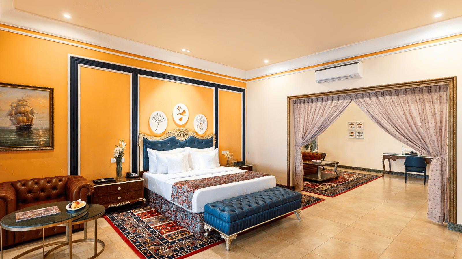 Suite with a king bed, a tufted bench, a leather sofa, coffee tables and an adjoining room through a gilded archway at MAYFAIR Palm Beach Resort, Gopalpur-on-Sea.
