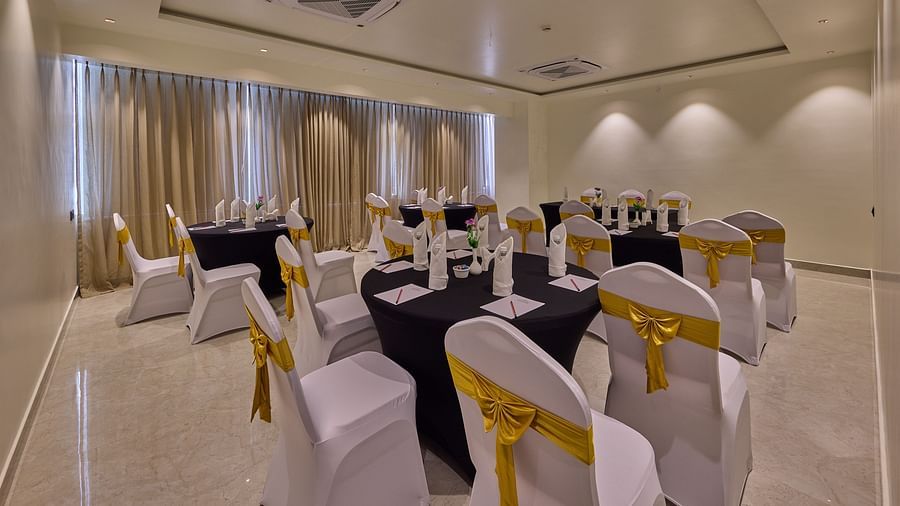 A banquet hall featuring chairs adorned in white covers and round tables with navy blue cloths, all bathed in ambient lighting