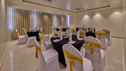 A banquet hall featuring chairs adorned in white covers and round tables with navy blue cloths, all bathed in ambient lighting