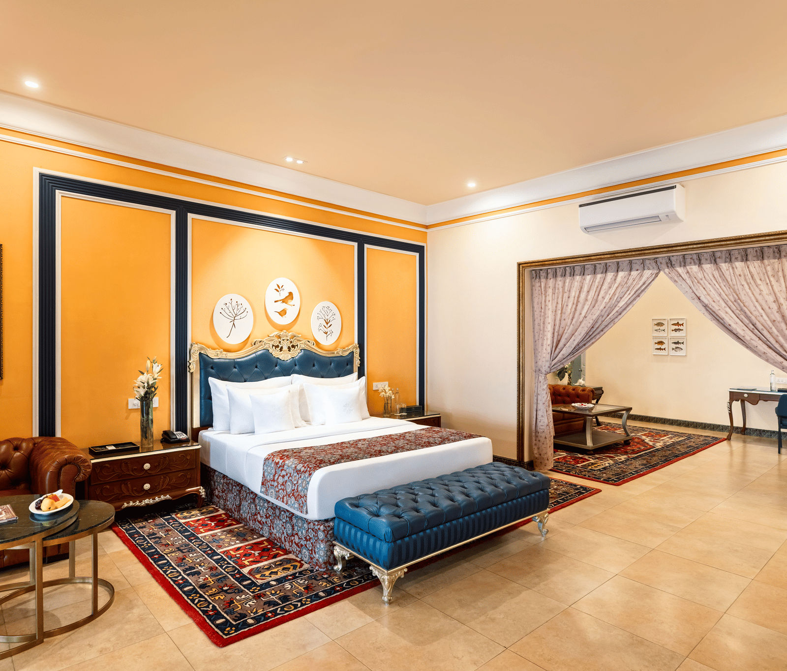 Suite with a king bed, a tufted bench, a leather sofa, coffee tables and an adjoining room through a gilded archway at MAYFAIR Palm Beach Resort, Gopalpur-on-Sea.