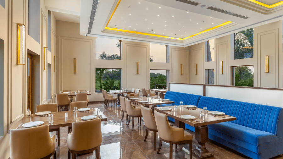 Restaurant at EsthereaRaj Leela, Ranakpur, featuring arranged tables and chairs with sunlight coming through tall vertical windows.