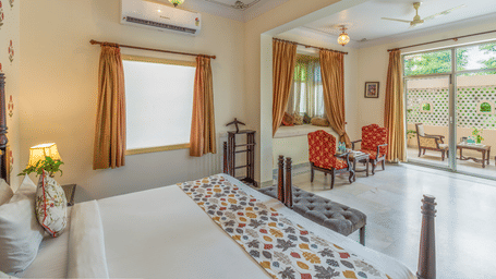 A bedroom with twin beds, a sitting area with chairs and glass doors opening to a balcony at Akshay Niwas Boutique Hotel By Amantra, Udaipur.