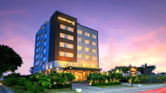 An image of the hotel building illuminated with bright yellow lights and a pink coloured sunset in the background - Golden Tulip, Agra