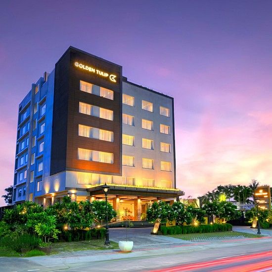 An image of the hotel building illuminated with bright yellow lights and a pink coloured sunset in the background - Golden Tulip, Agra