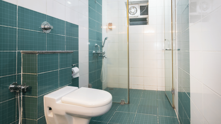 Bathroom with teal mosaic tiles, a shower area, and a toilet at Sanctum Suites Indiranagar, Bangalore.