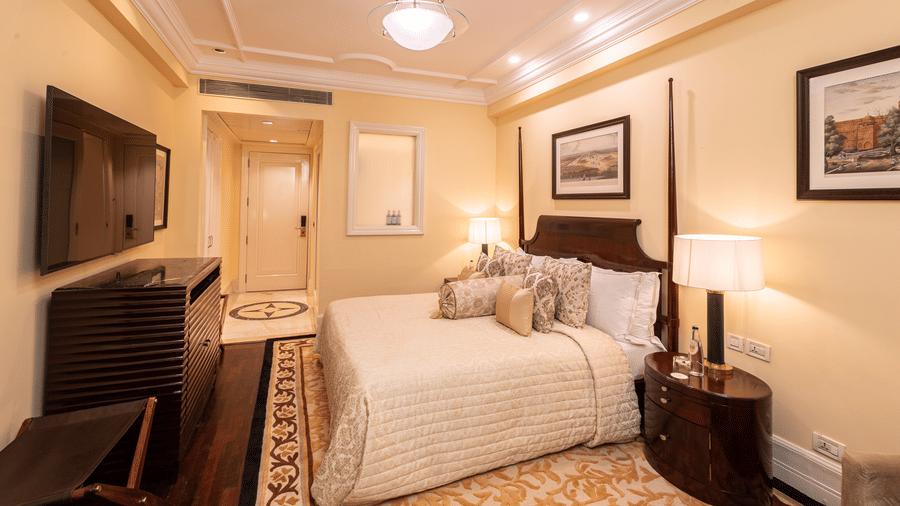 image of our heritage parlour room from a corner angle showing the plush soft bed and a wall mounted television placed in front of it - The Claridges New Delhi