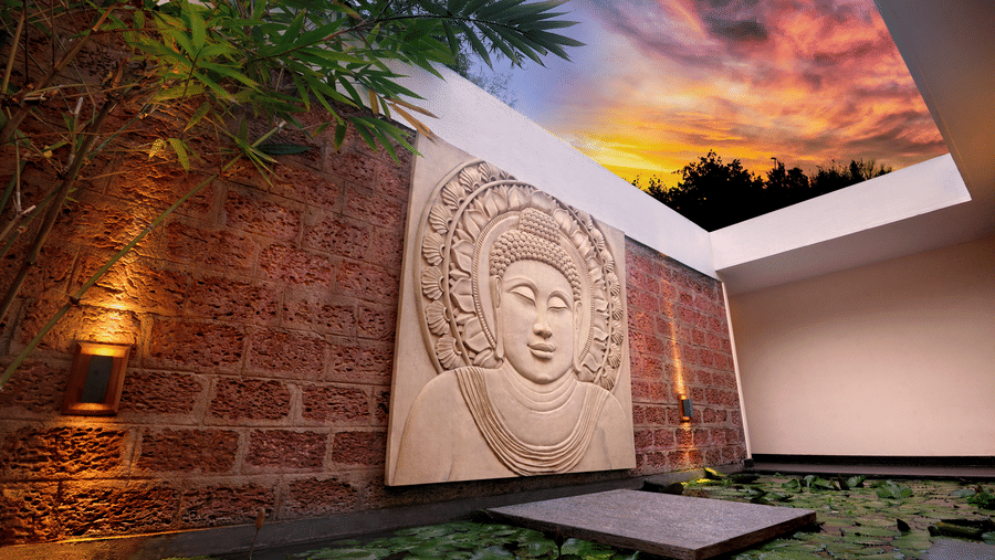 Stone Buddha carving on a textured wall overlooking a lily pond with a twilight sky at Amanvana Spa Resort - A Luxury Resort in Coorg.