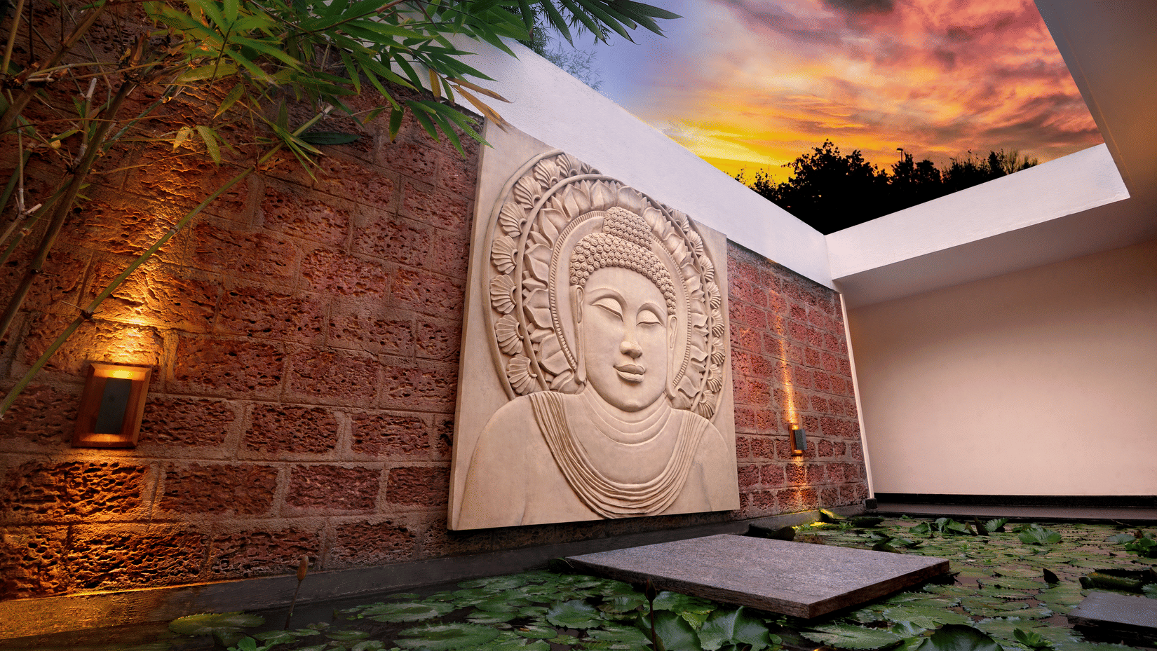 Stone Buddha carving on a textured wall overlooking a lily pond with a twilight sky at Amanvana Spa Resort - A Luxury Resort in Coorg.