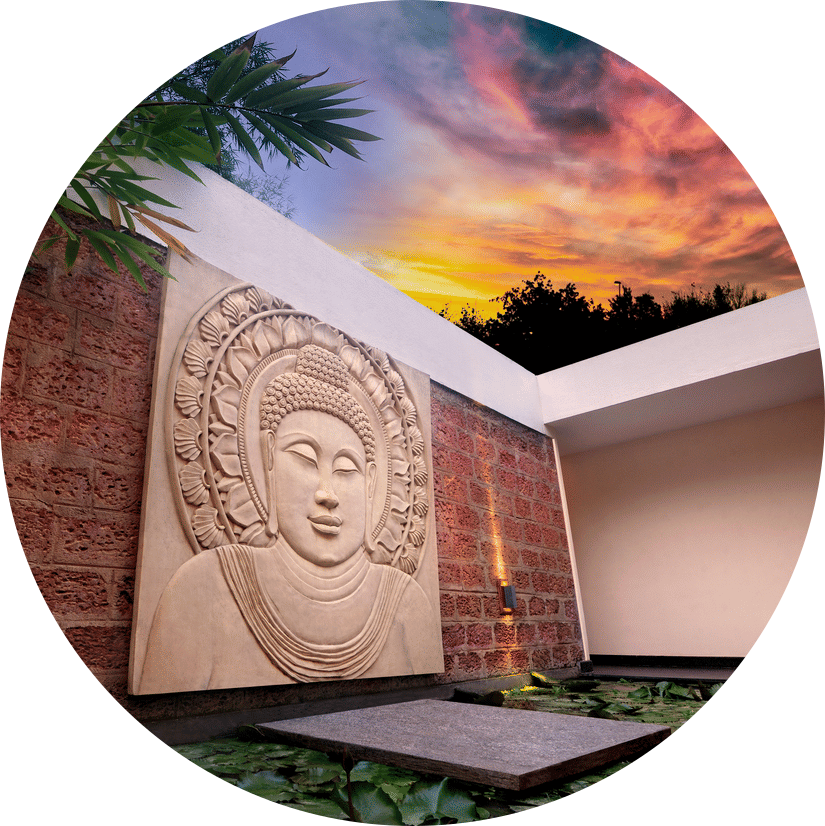 Stone Buddha carving on a textured wall overlooking a lily pond with a twilight sky at Amanvana Spa Resort - A Luxury Resort in Coorg.