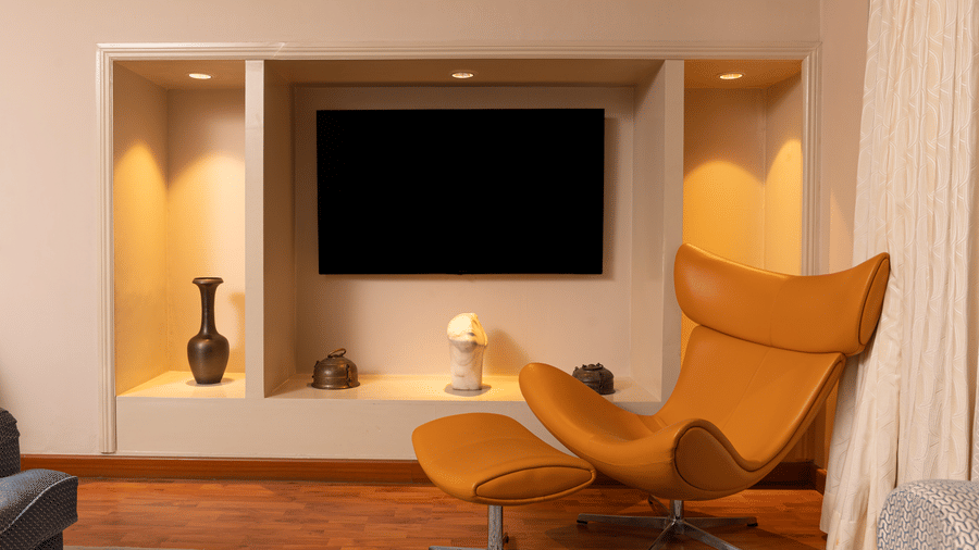 an image from the living room of the regent suites with a wall mounted tv and a occur yellow chair - The Claridges New Delhi