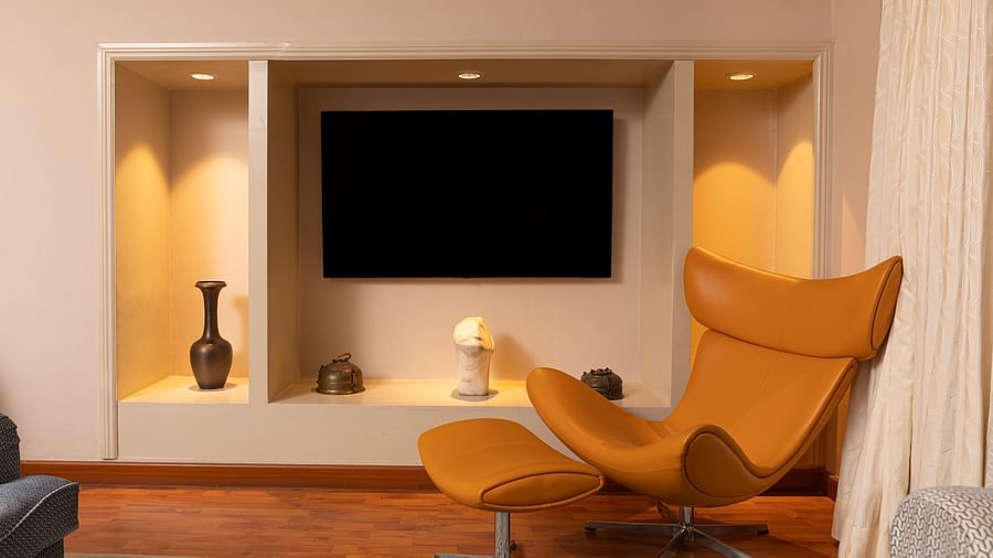 an image from the living room of the regent suites with a wall mounted tv and a occur yellow chair - The Claridges New Delhi