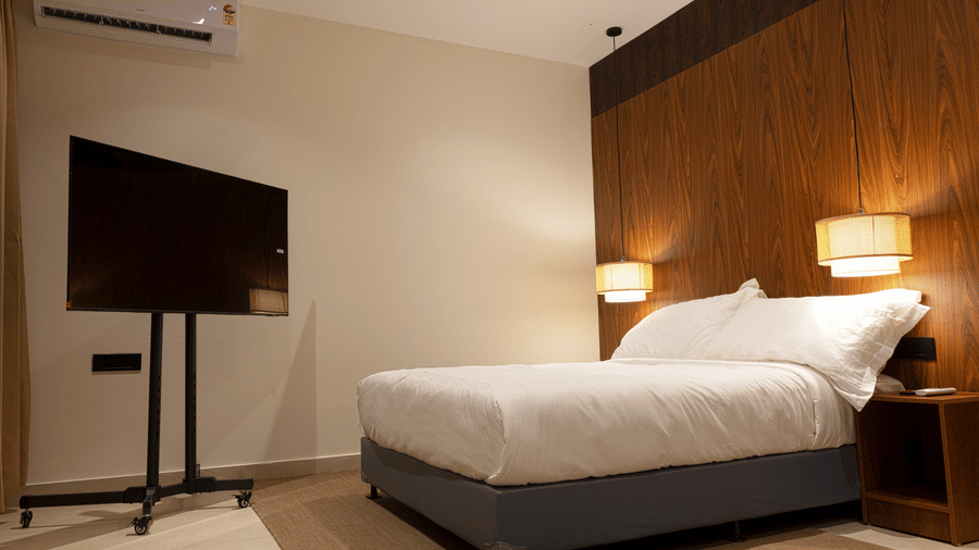 Hotel room at SUKAVI with a large bed, nightstands, lamps, a wall-mounted air conditioner, and a television on a stand.