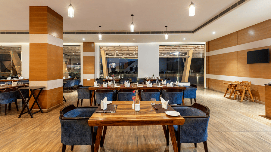 Gulmohar Rasoi, at Via Lakhela Resort & Spa, is one of the best places to eat in Kumbhalgarh, featuring a dining area with wooden tables, blue chairs, and decorative walls.