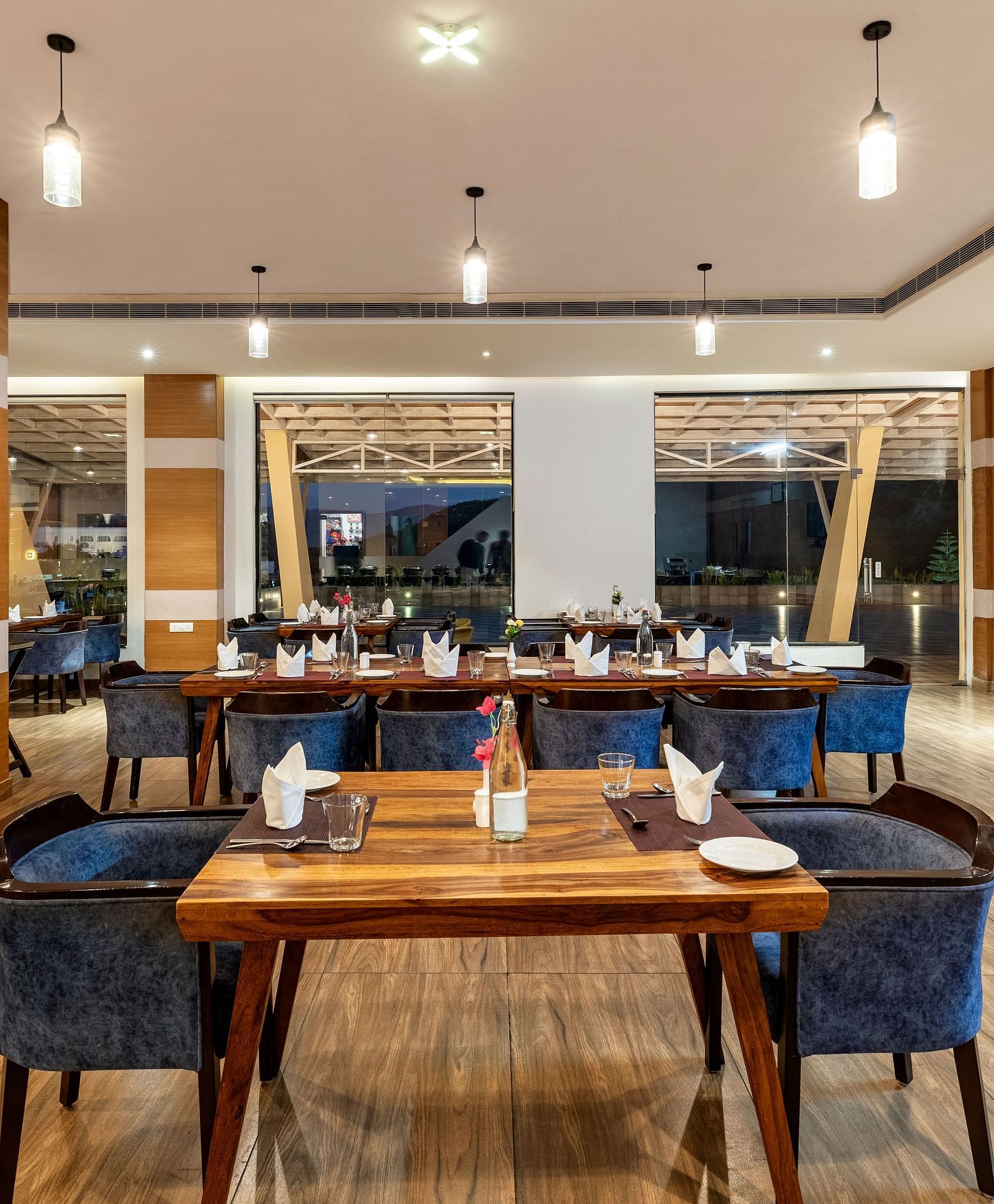 A dining area with tables and chairs, set with place settings, and hanging lights - Via Lakhela Resort & Spa, Kumbhalgarh