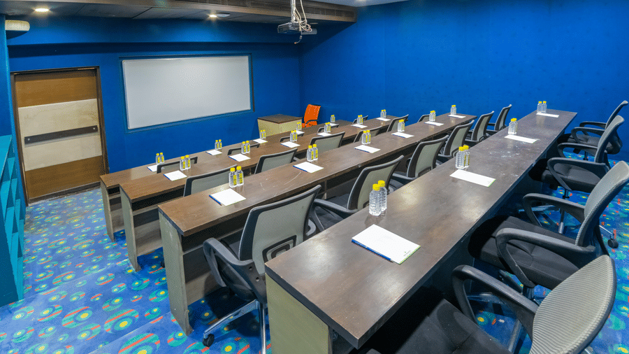 Modern boardroom with blue walls and a long conference table arranged in classroom style seating- Narayani Heights Hotel & Resorts
