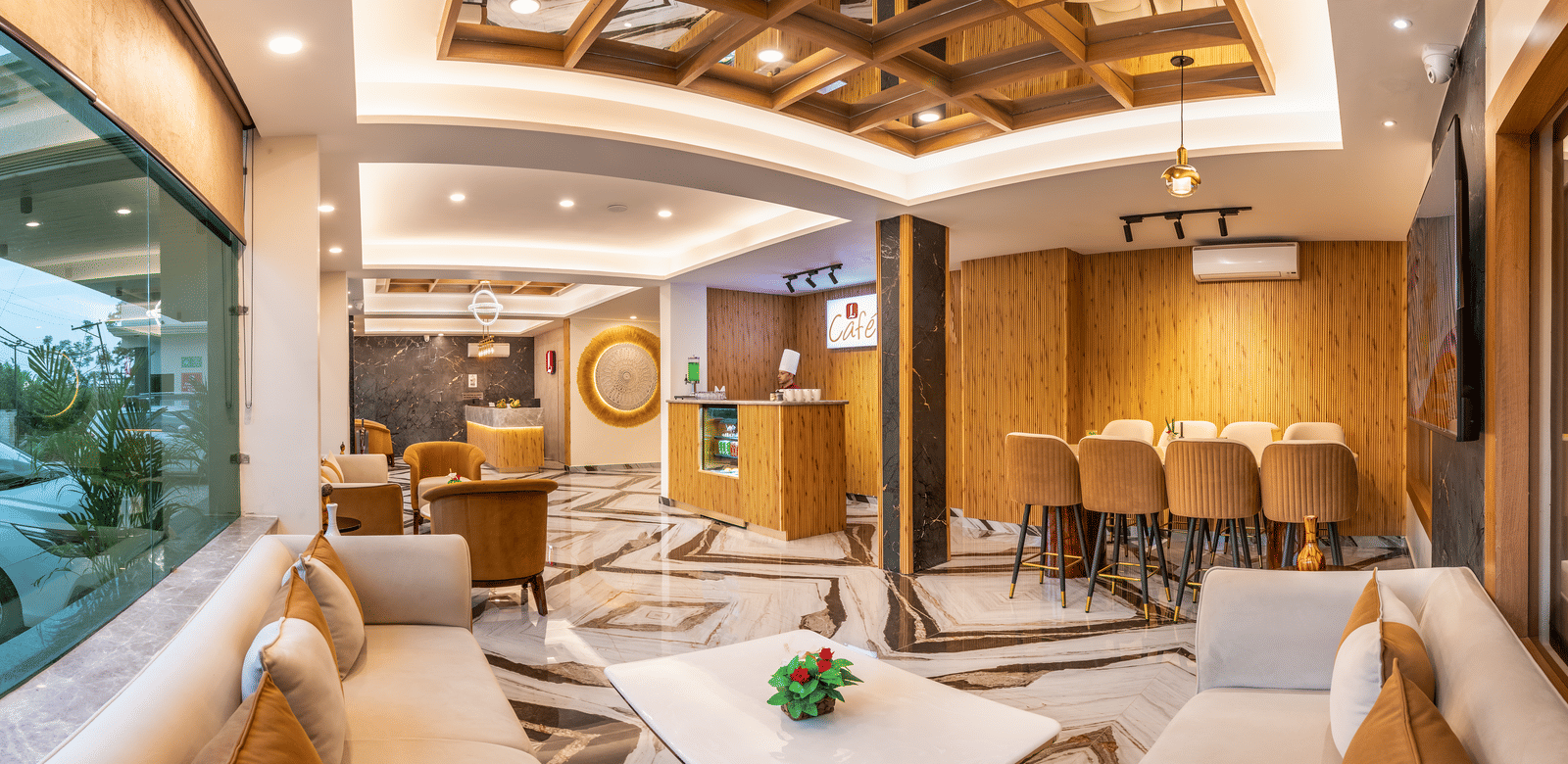The lobby lounge at Lords Inn Katra features sofa seating, a decorative wooden ceiling panel, and large glass windows.