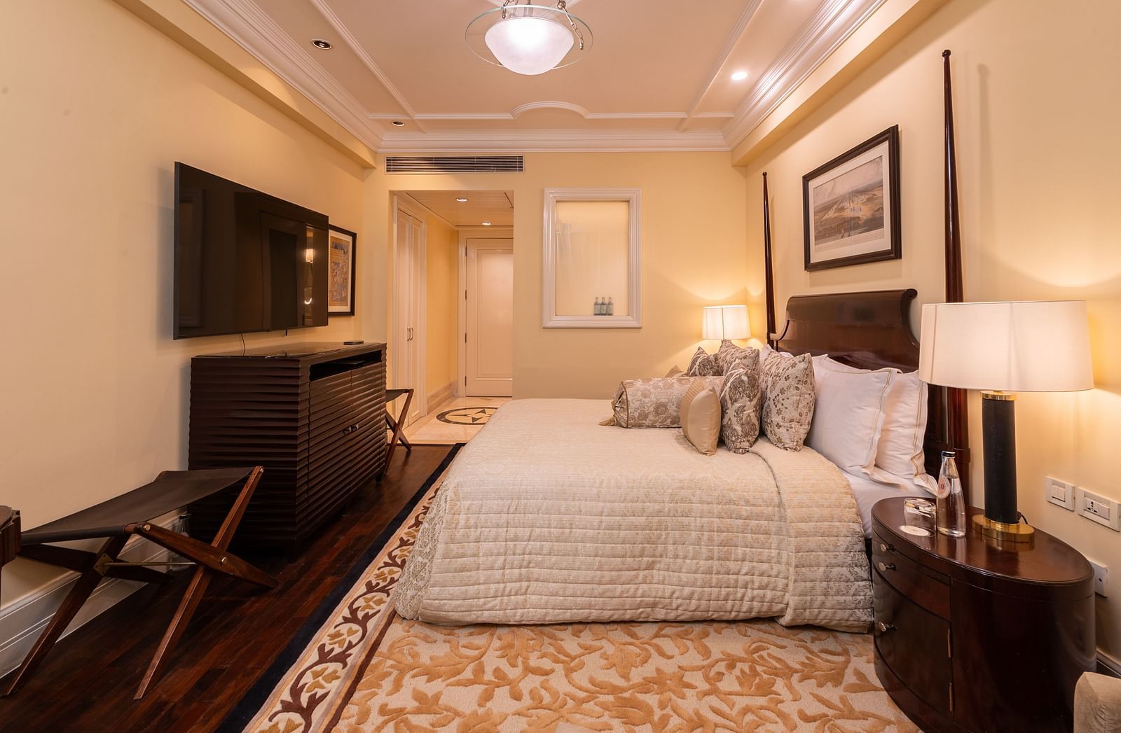 side view of the the heritage parlour room with a view of the king size bed with white sheets and the corridor with entrance door at the far corner of the room - The Claridges New Delhi